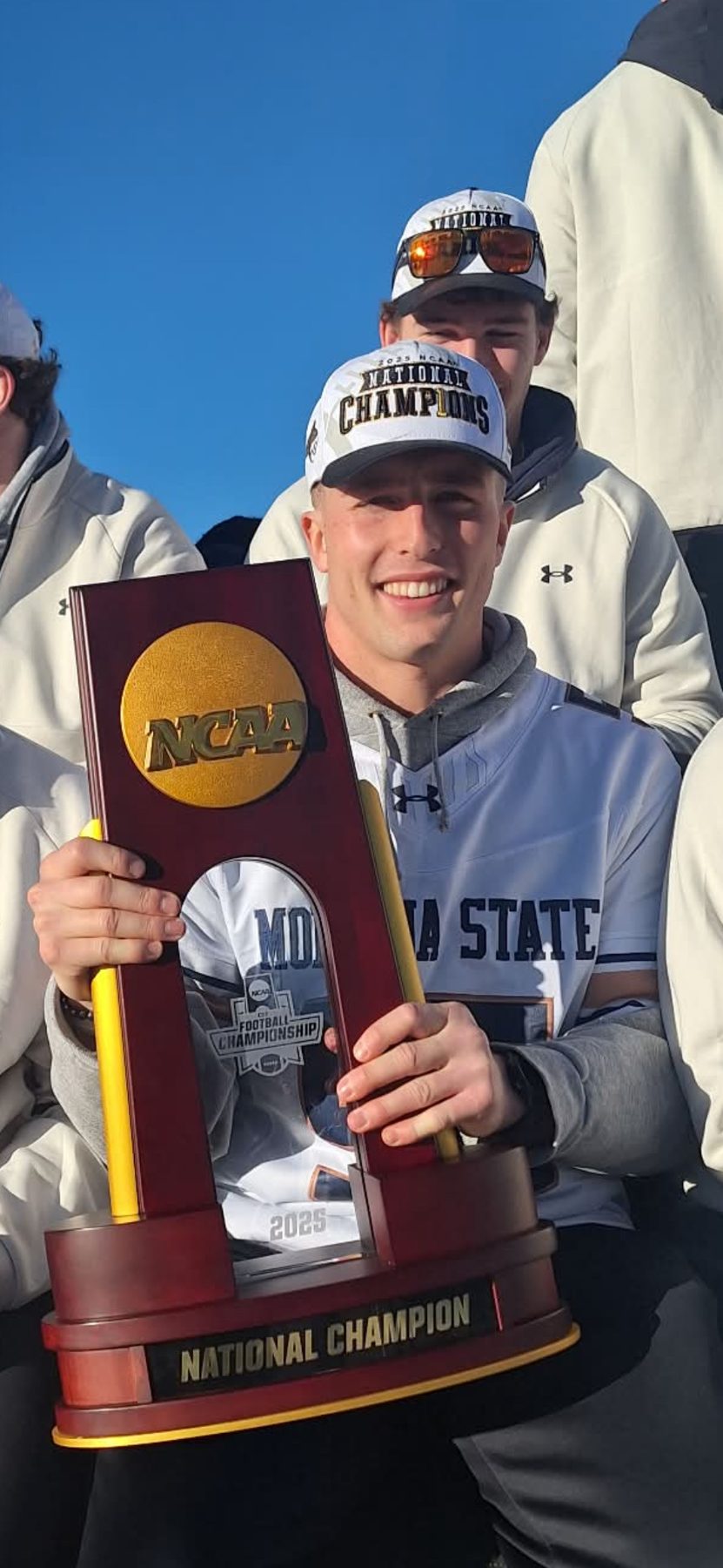A Bobcat in a National Champions cap holds the NCAA FCS National Champion trophy