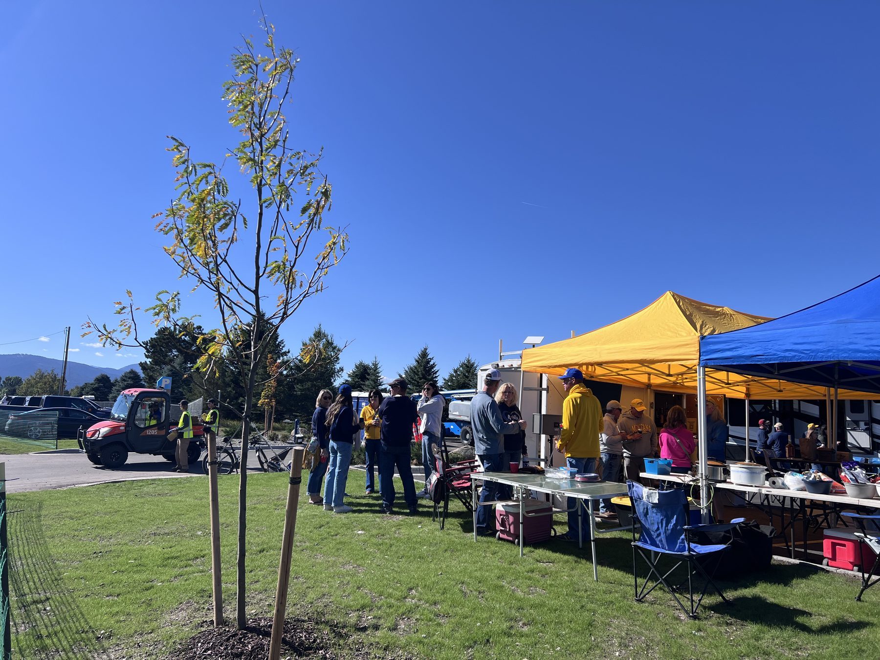 Blue and gold tailgate tents with fans and the Bridger mountains behind on a Bozeman gameday